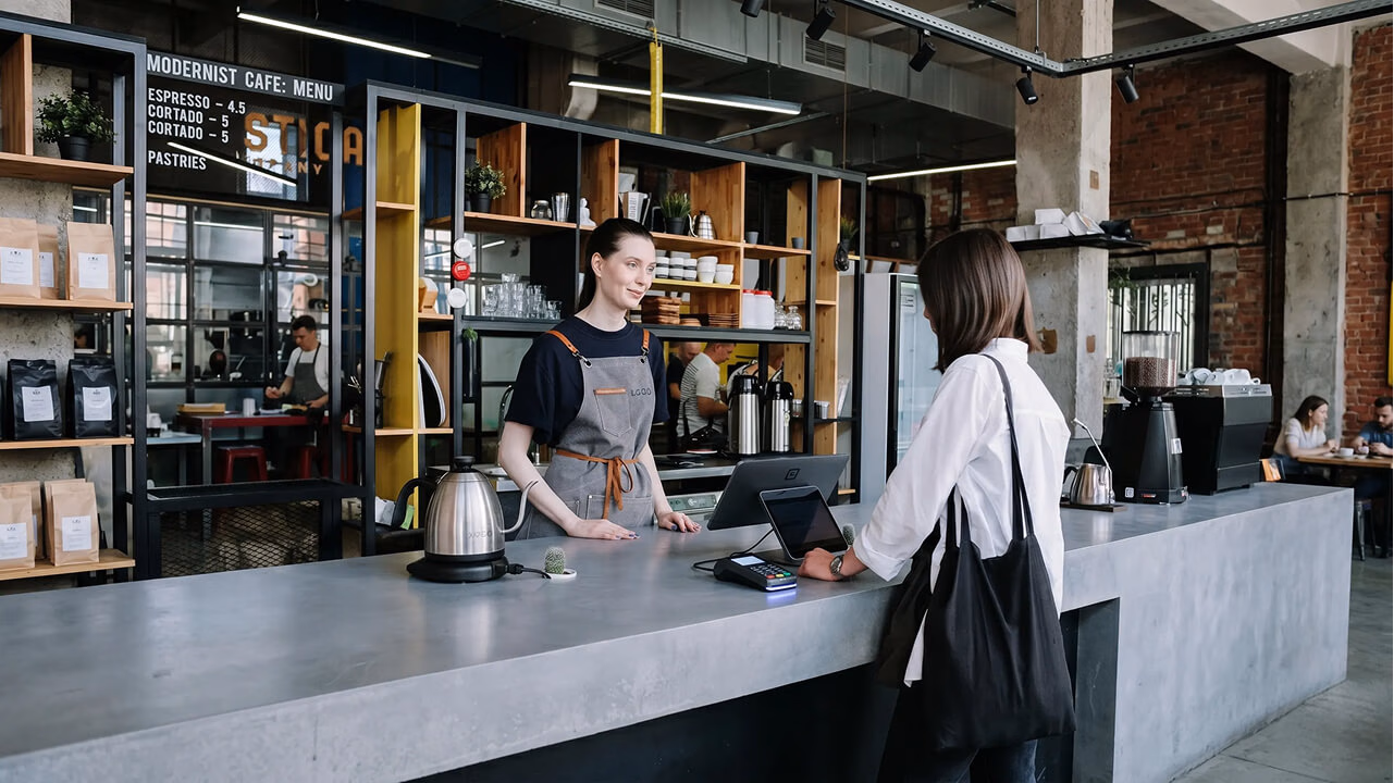Customers and a barista in a coffee shop setting demonstrating point-of-sale device management.