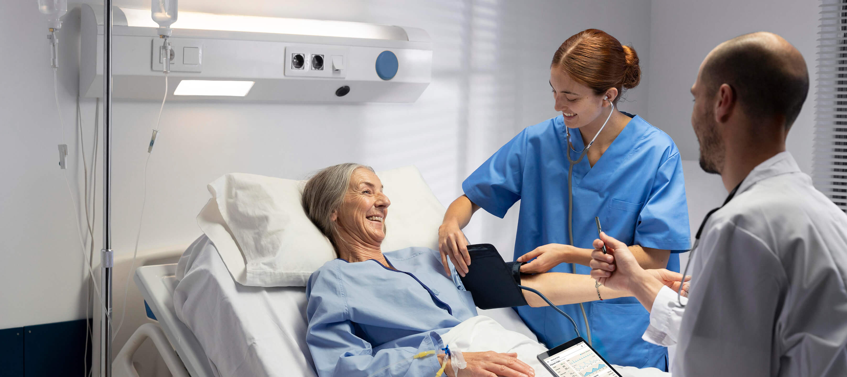 Healthcare professionals using an Android medical tablet next to a patient in a hospital room, demonstrating secure shared device management and HIPAA-compliant endpoint data security.