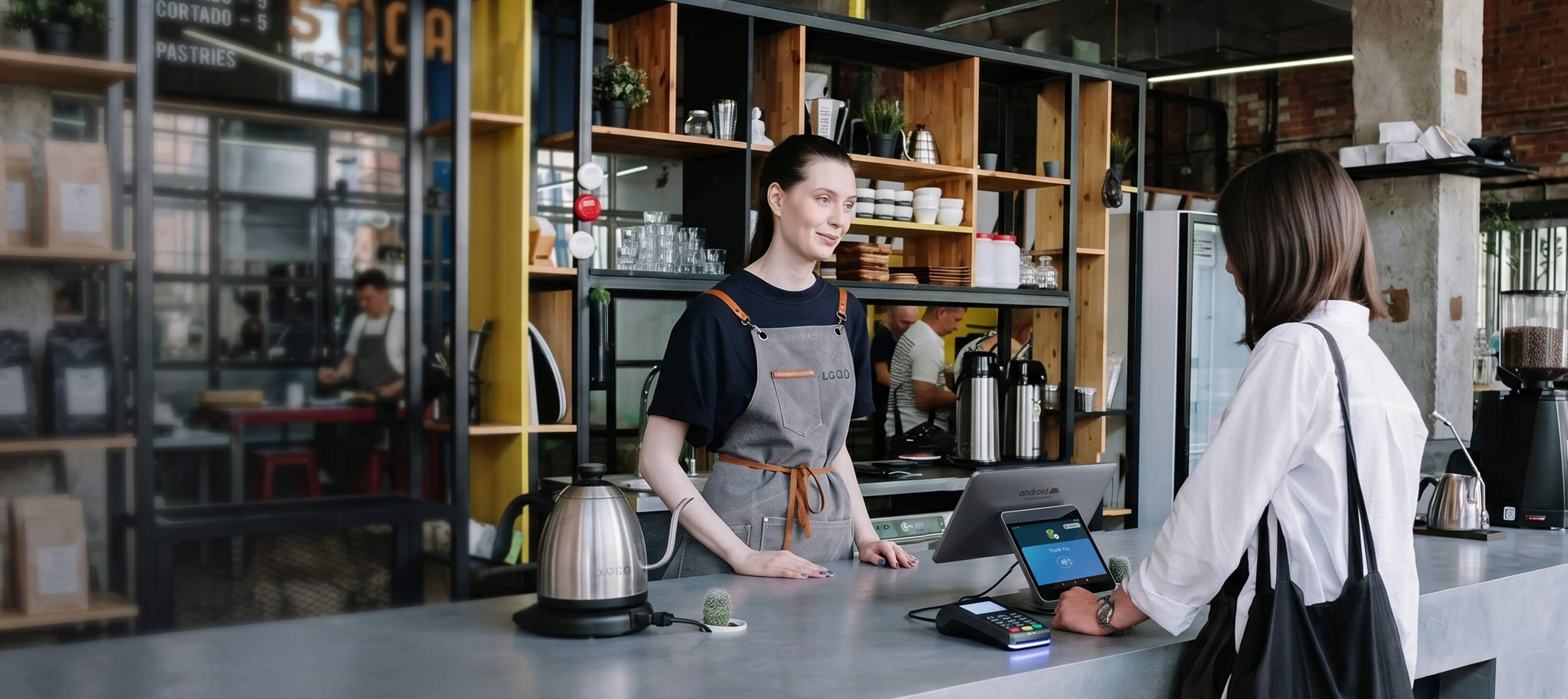 A cafe barista behind a modern counter processing transactions on an Android point-of-sale terminal tablet, illustrating enterprise retail kiosk software lockdown and secure hospitality configurations.